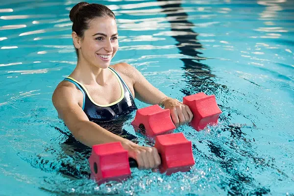 Femme exerçant avec haltères en mousse dans une piscine